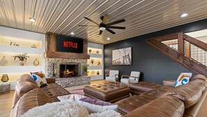 Sala moderna com lareira de pedra, sofás de couro e sinal da Netflix.