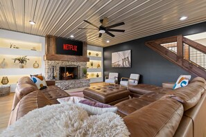 A modern living room with a stone fireplace, leather sofas, and a Netflix sign. - Mtn Views Theater Hot Tub 5 King Suites (Blue Ridge)
