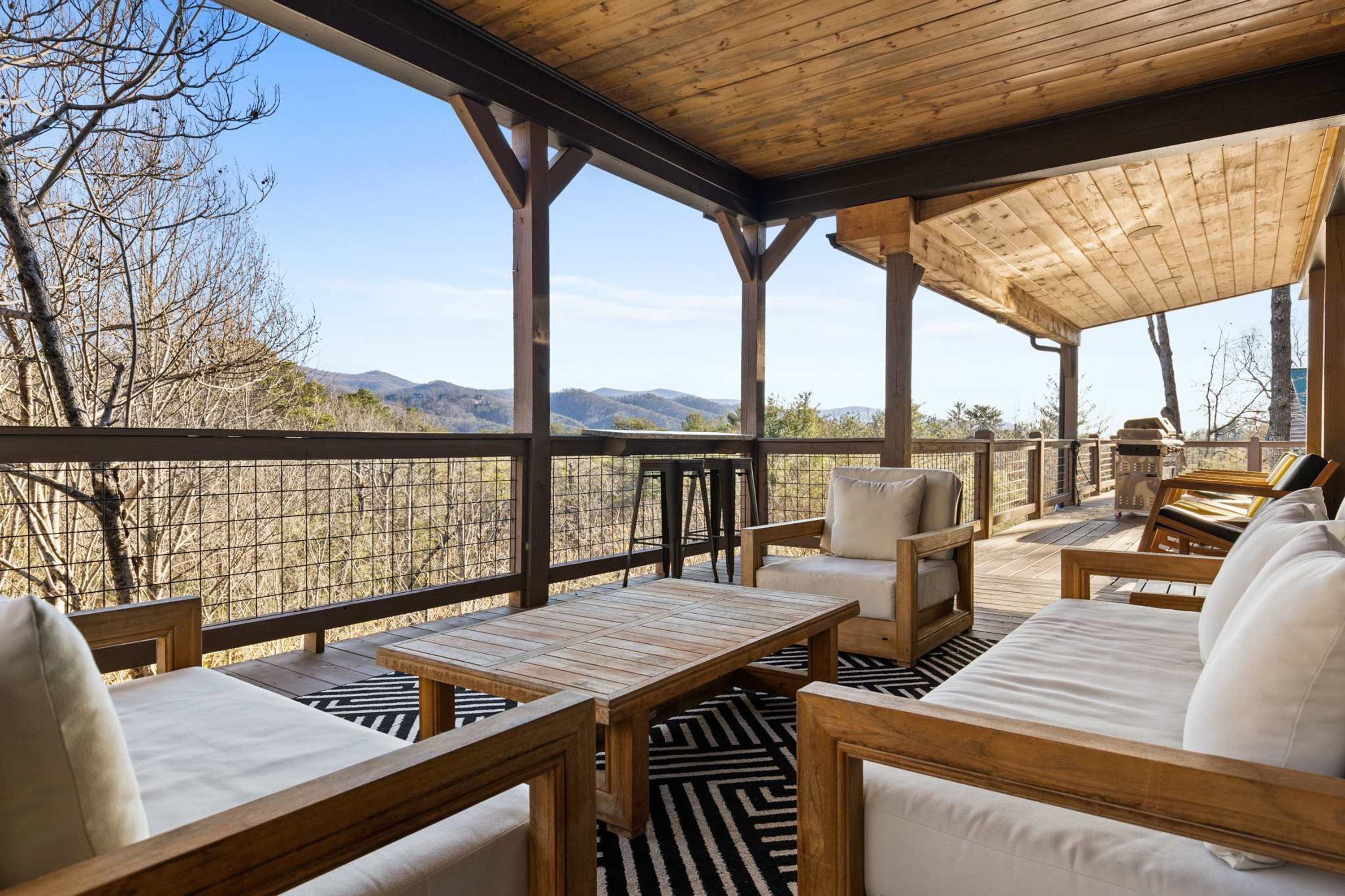 A covered outdoor seating area with wooden furniture and a view of mountains.