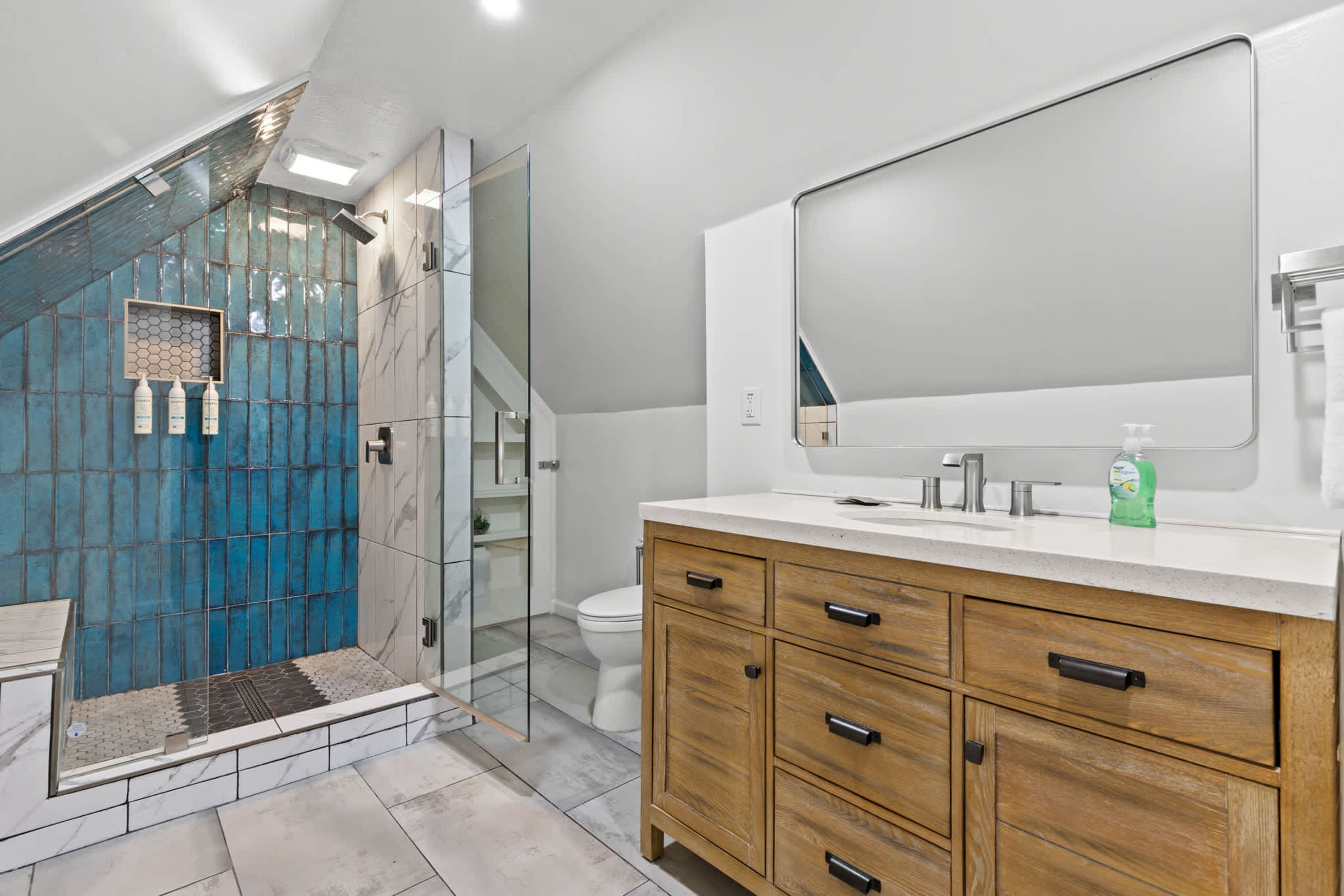 A modern bathroom with a shower, toilet, vanity, and a large mirror.