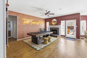 A pool table in a room with a neon sign, a ceiling fan, and a fireplace. - Upscale Escape Pool Hot Tub Game Room Firepit (San Antonio)
