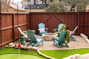 A backyard with a wooden fence, a fire pit, and four Adirondack chairs with cushions. - Upscale Escape Pool Hot Tub Game Room Firepit (San Antonio)