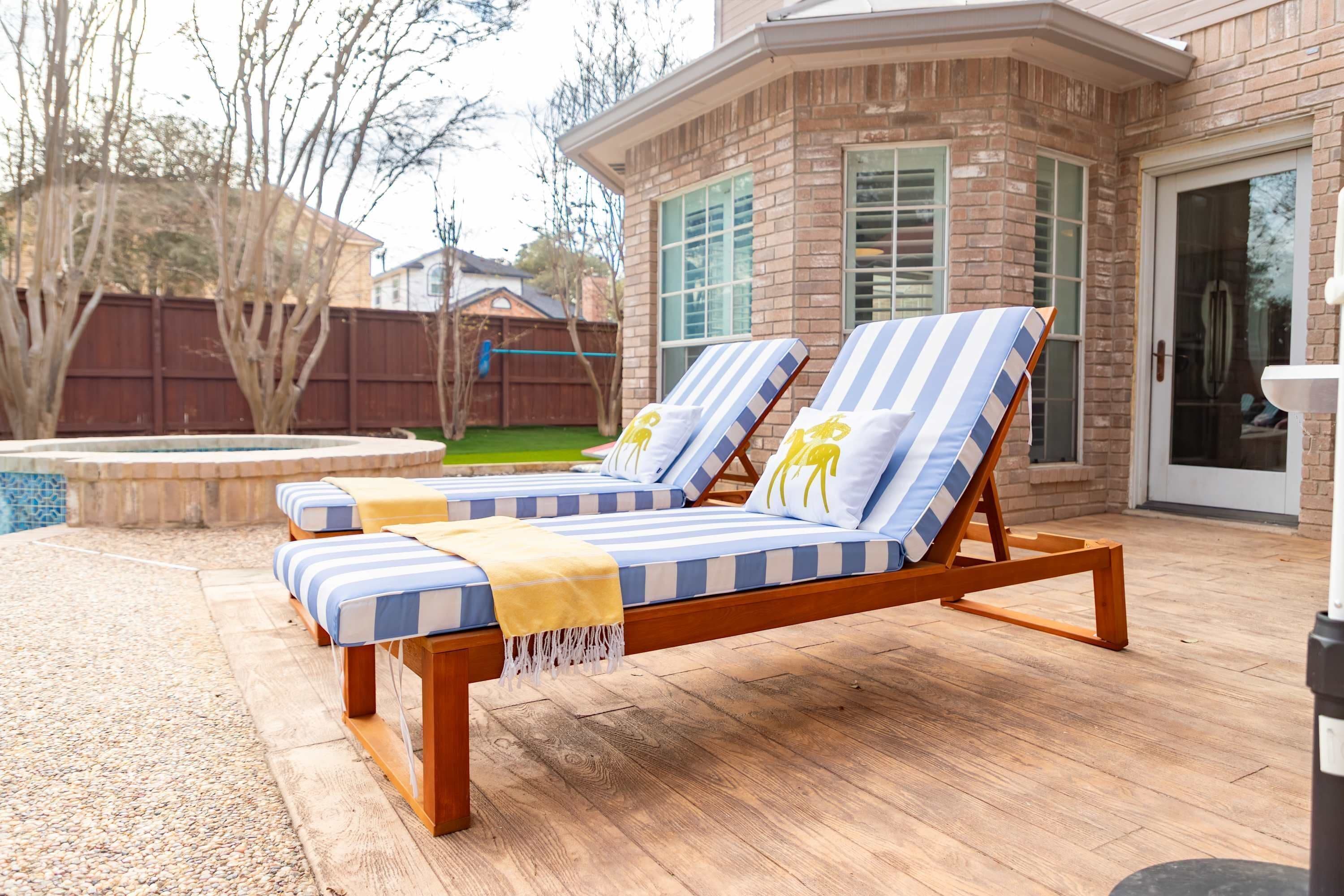A deck with two lounge chairs, a small pool, and a brick house in the background.