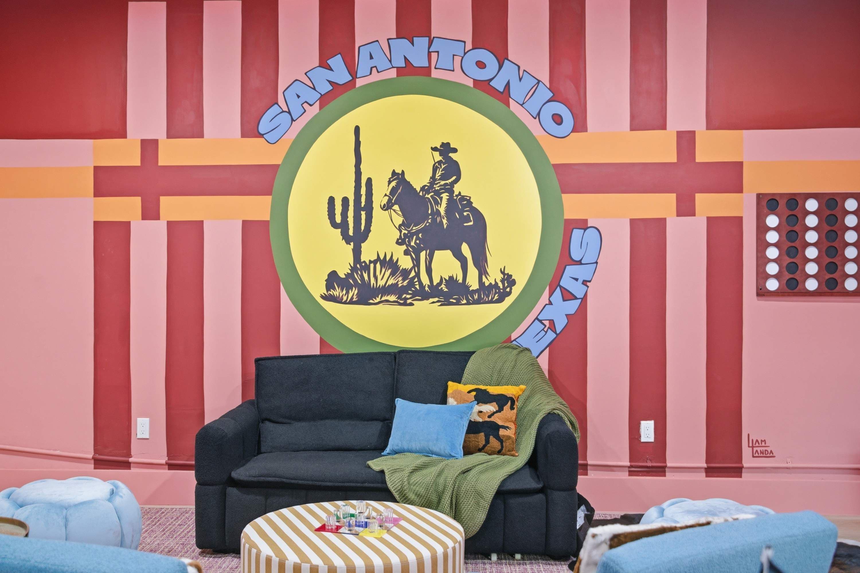 A room with a sofa, ottoman, and a wall with a circular emblem featuring a cowboy and cactus.