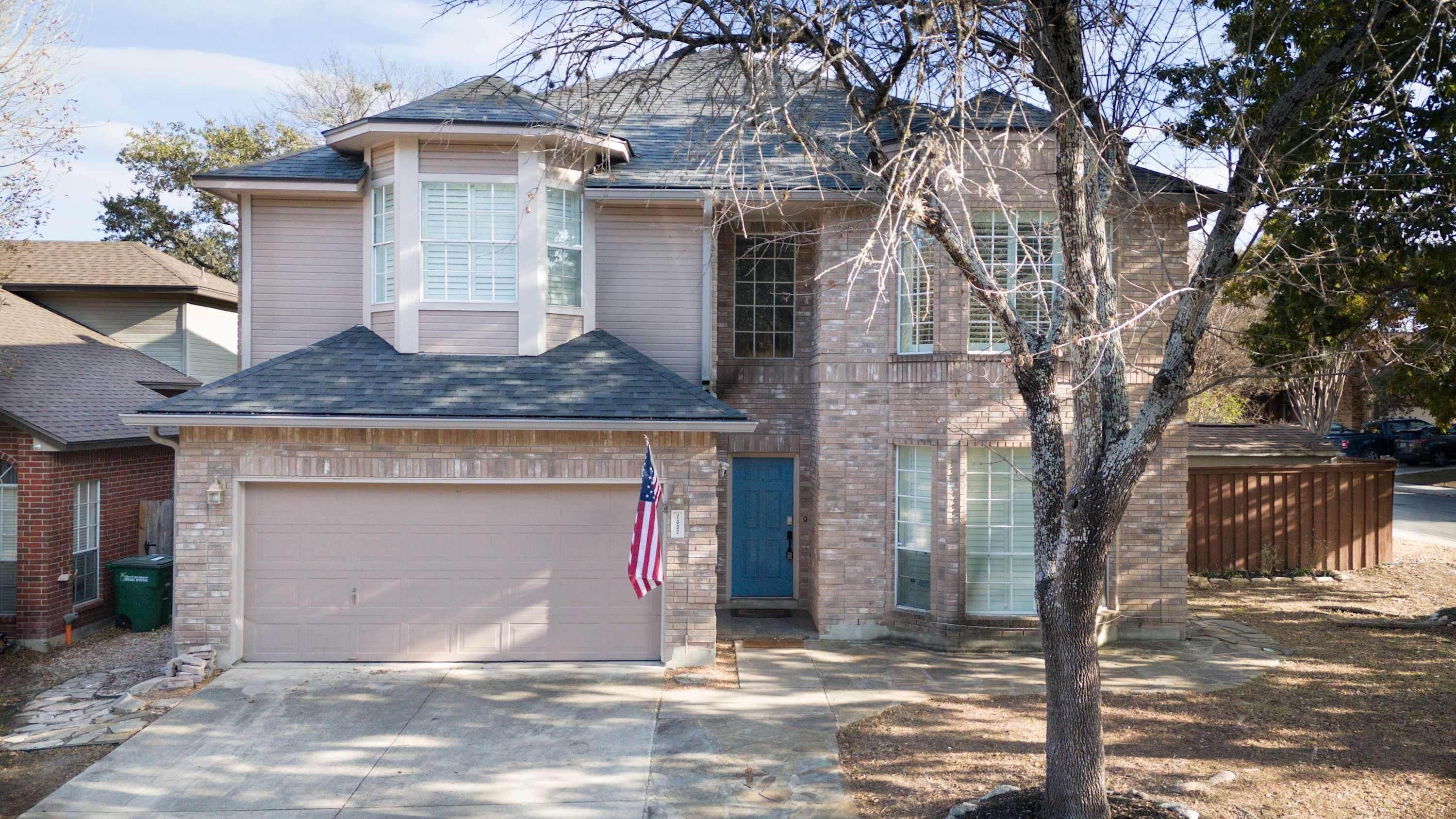 A two-story house with a garage, a front door, and a tree in the yard.