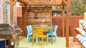 Eine Außenpatio mit einer Holz-Pergola, einem Grill, einem Tisch mit Stühlen und einem Schachbrettboden.