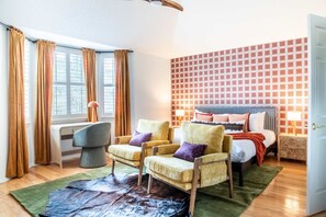 Une chambre d’hôtel comprenant un lit, deux fauteuils, un bureau, une fenêtre avec des rideaux, un mur à motifs et un tapis.