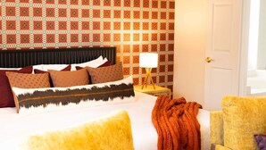 Ein Hotelzimmer mit strukturiertem Wandpapier, einem Bett mit vielen Kissen, einer Nachttischlampe und einer Tür.