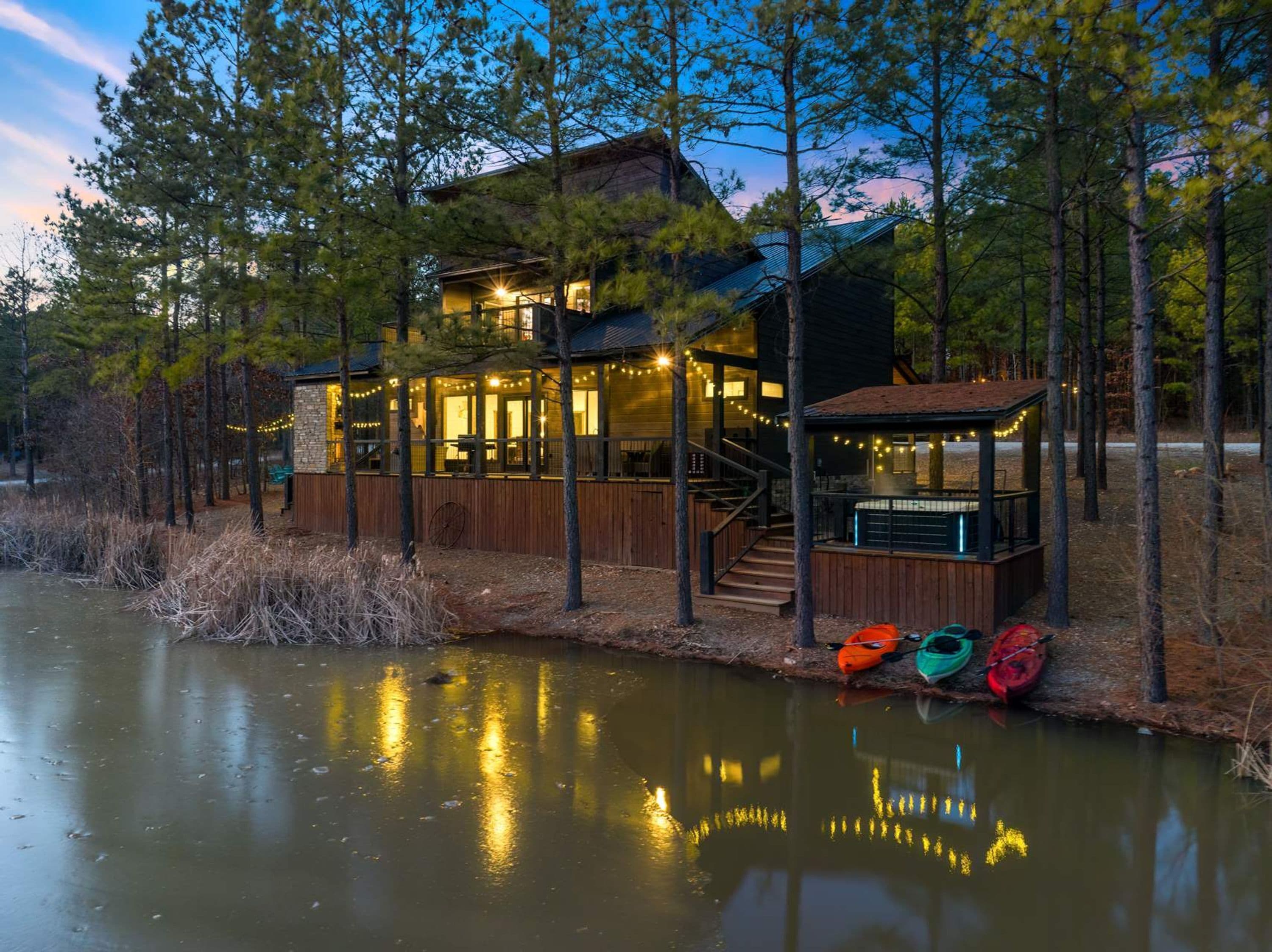 A lakeside cabin with a deck, a covered outdoor area, and a dock with kayaks.