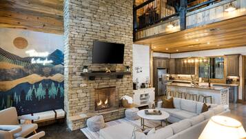 A spacious living area with a stone fireplace, a large flat-screen TV mounted on the wall, and a cozy seating arrangement.