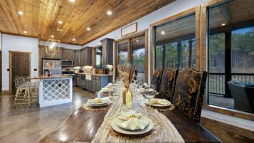 A spacious dining area with a long table set for a meal, large windows offering a view of the outdoors, and a kitchen area with modern appliances.