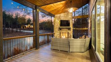 A covered outdoor area with a stone fireplace, seating, and a television.