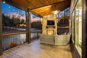 A covered outdoor area with a stone fireplace, seating, and a television.