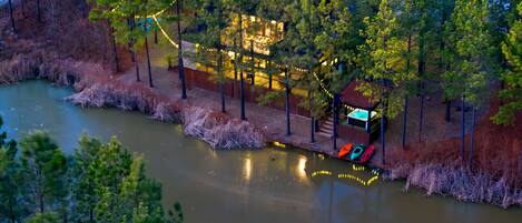 A riverside property with a dock, boats, and a building with string lights.