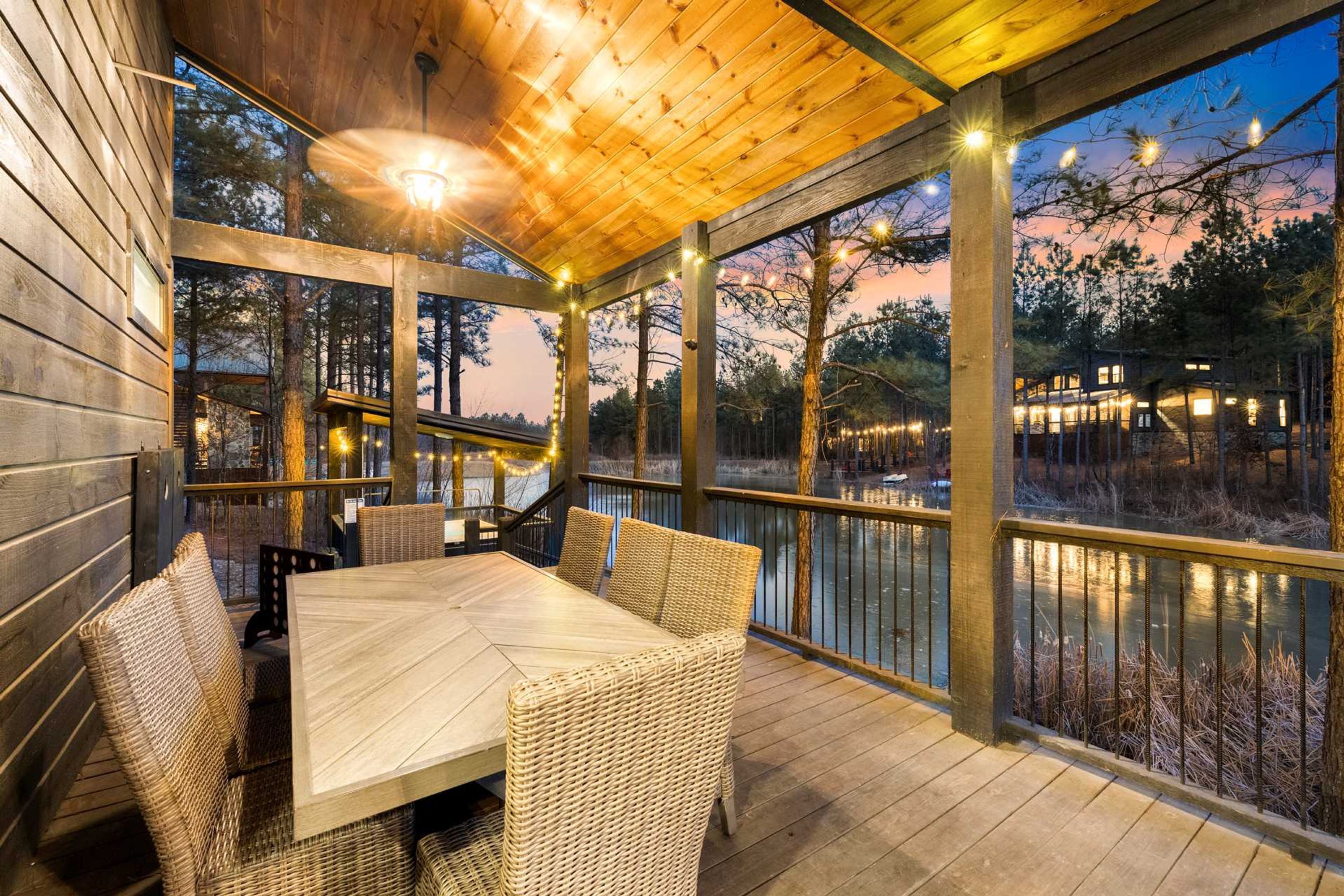 A covered outdoor area with a wooden deck, wicker furniture, and string lights.