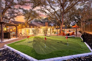 Een goed onderhouden golfbaan met een putting green, omringd door bomen en een houten hek.