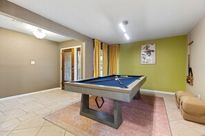 Ein Billardtisch in einem Raum mit Tür, einem Vorhangfenster und einem Gemälde an der Wand.