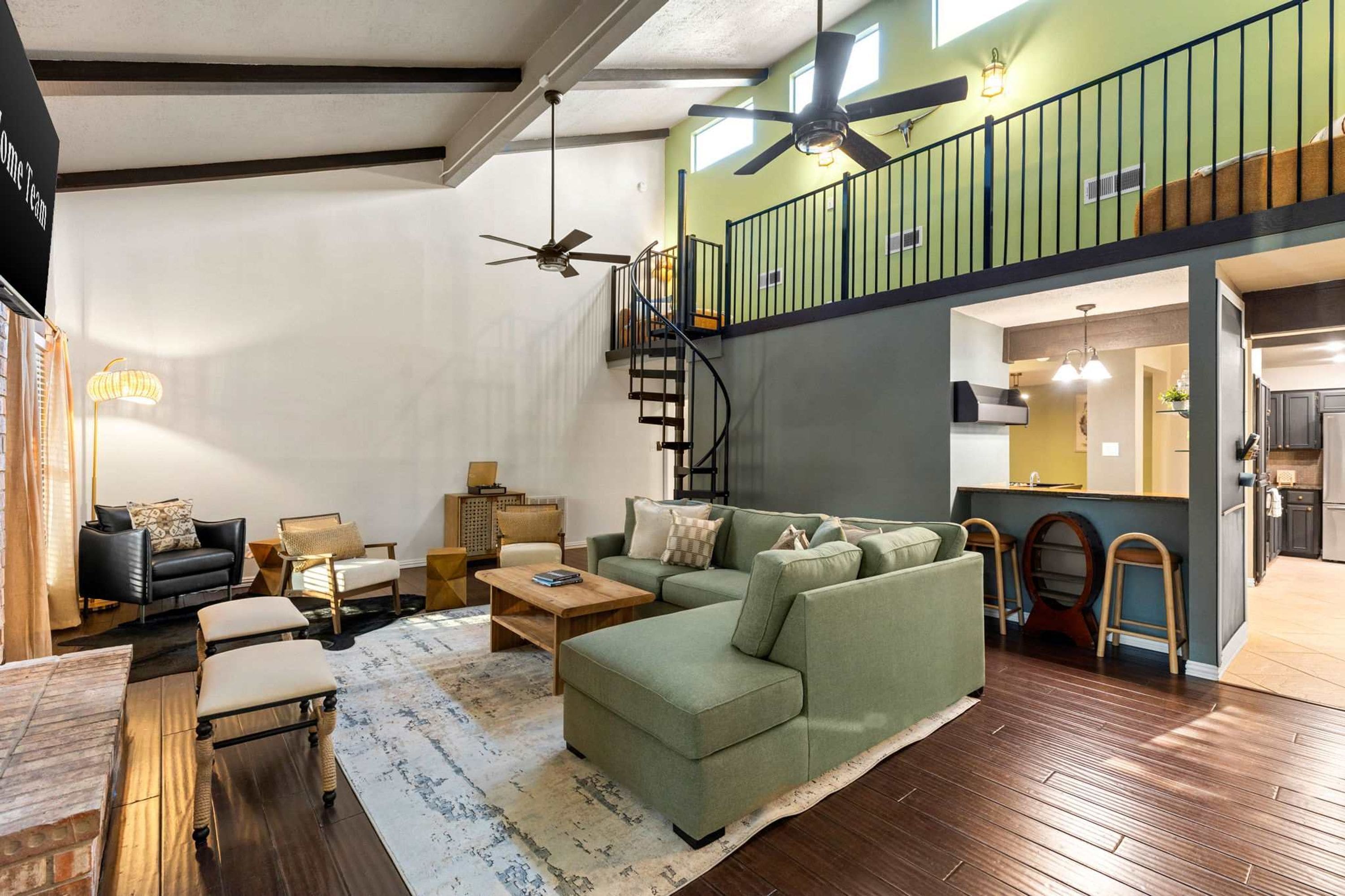 A spacious living room with a green sofa, a wooden coffee table, and a staircase leading to an upper level.