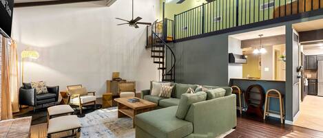A spacious living room with a green sofa, a wooden coffee table, and a staircase leading to an upper level.