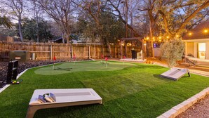 Ein Garten mit Putting-Grün, einer Holzterrasse und einem überdachten Sitzbereich.