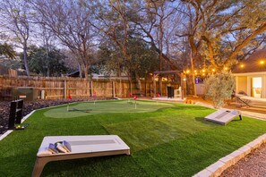 Ein Garten mit Putting-Grün, einer Holzterrasse und einem überdachten Sitzbereich.
