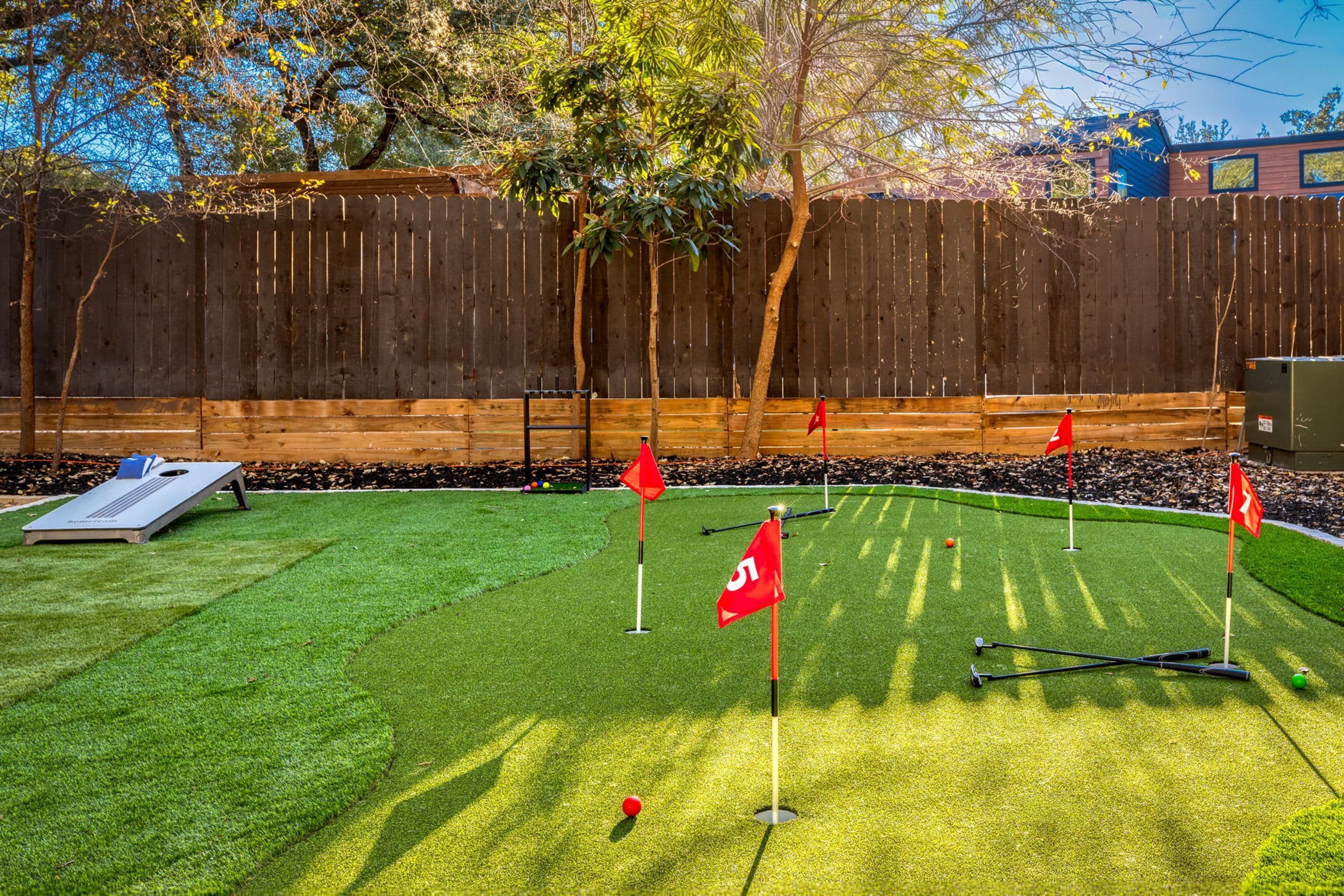 A backyard with artificial grass, a putting green, and a wooden fence.