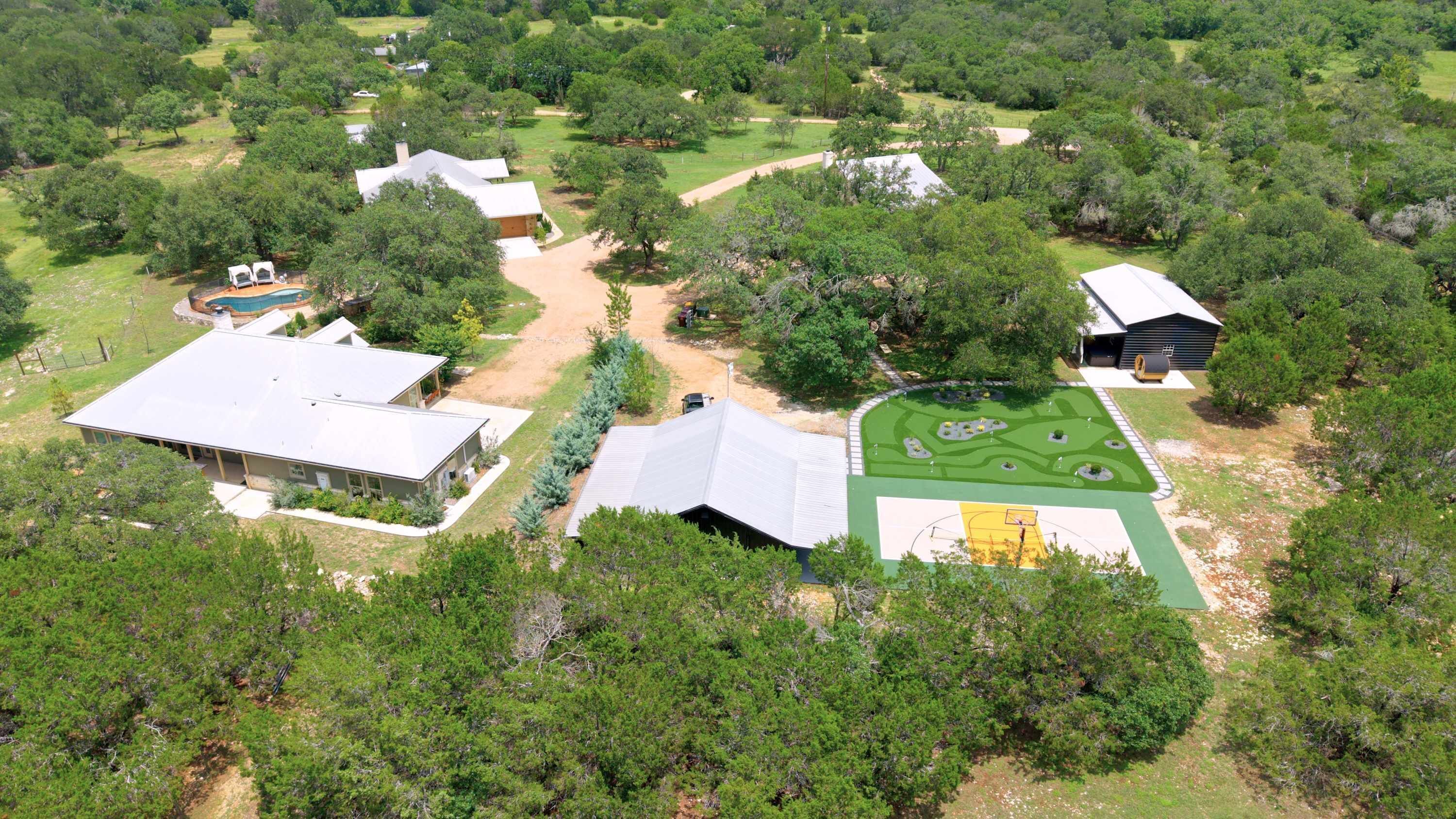An aerial view of a residential property with multiple buildings, a basketball court, and surrounding greenery.