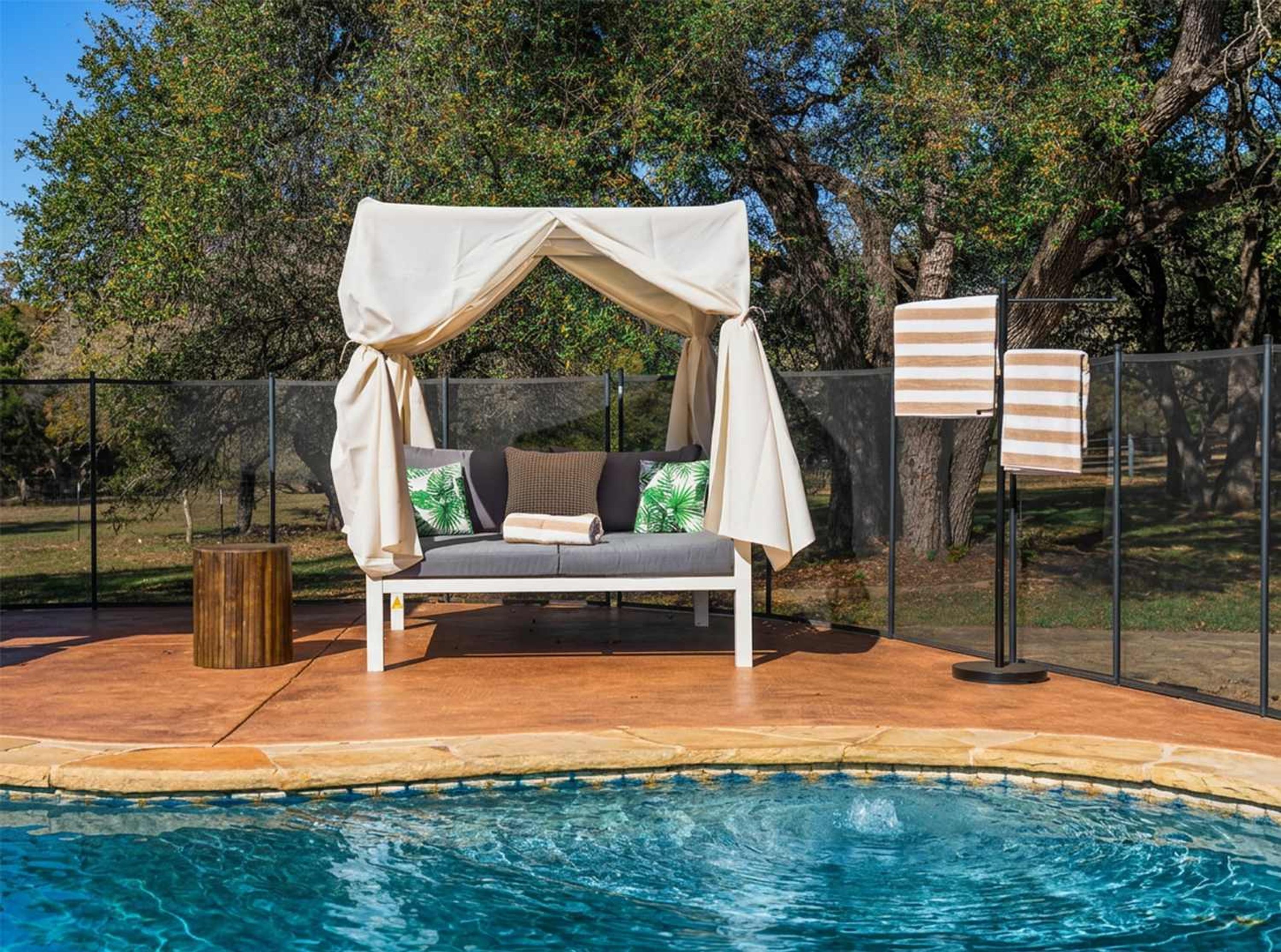 A poolside seating area with a canopy, a pool, and a fence.