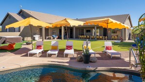 A poolside area with lounge chairs, umbrellas, and a hot tub. - Suncrest Retreat - Pool Pickleball Theater (Scottsdale)