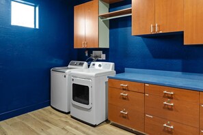 A laundry room with two washing machines, wooden cabinets, and a blue countertop. - Suncrest Retreat - Pool Pickleball Theater (Scottsdale)