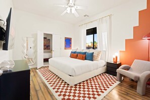 A bedroom with a bed, a nightstand, a chair, a window with curtains, a ceiling fan, and a door leading to another room. - Suncrest Retreat - Pool Pickleball Theater (Scottsdale)