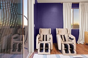 Une pièce équipée de deux fauteuils de massage, d’une grande fenêtre avec des rideaux et offrant une vue sur l’extérieur.