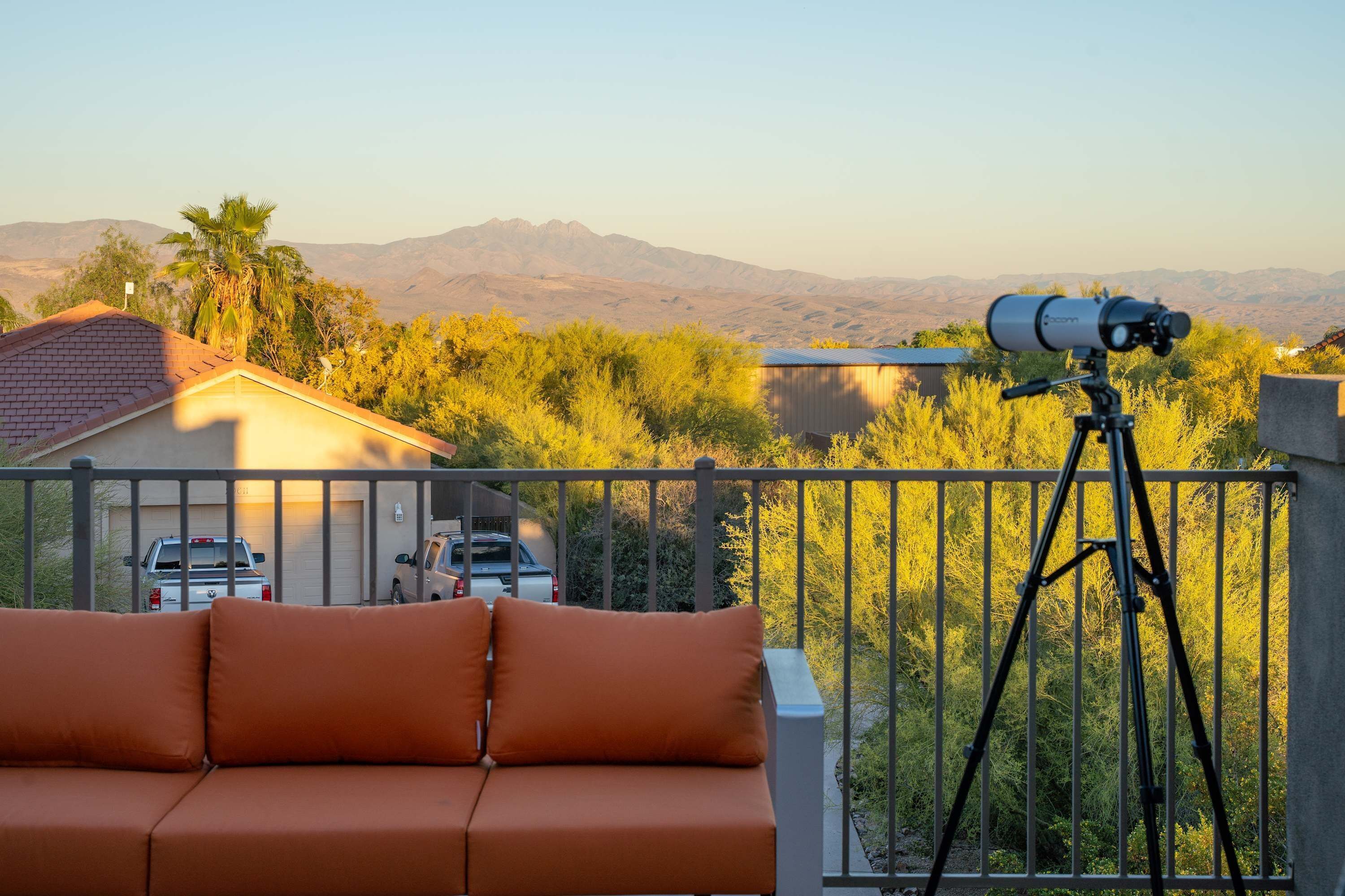 Un balcón con un telescopio, un sofá y vistas a montañas y árboles.