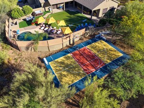 Vue aérienne d’une propriété résidentielle dotée d’une piscine, d’un patio couvert avec des meubles d’extérieur et d’un terrain de basketball.