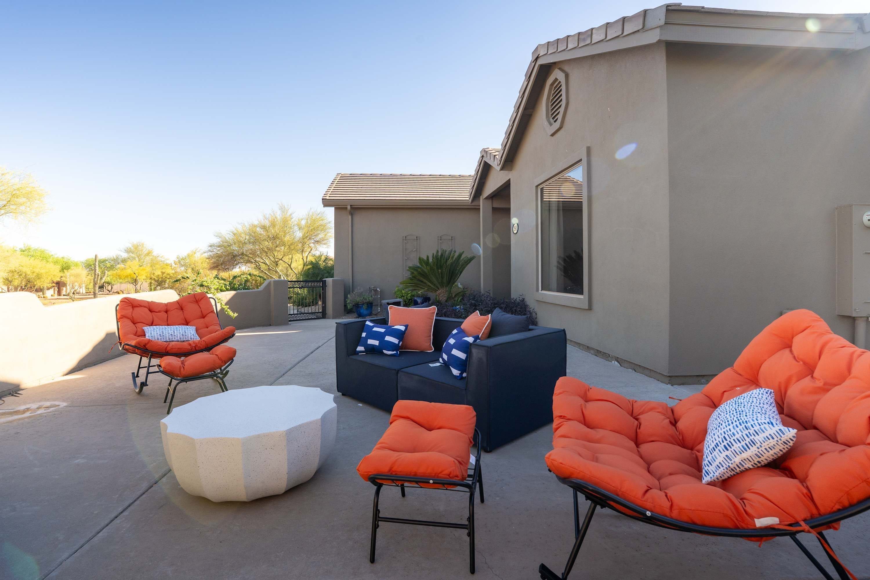Un espace patio aménagé avec du mobilier d’extérieur, notamment des chaises orange et un canapé, ainsi qu’une petite table ronde.