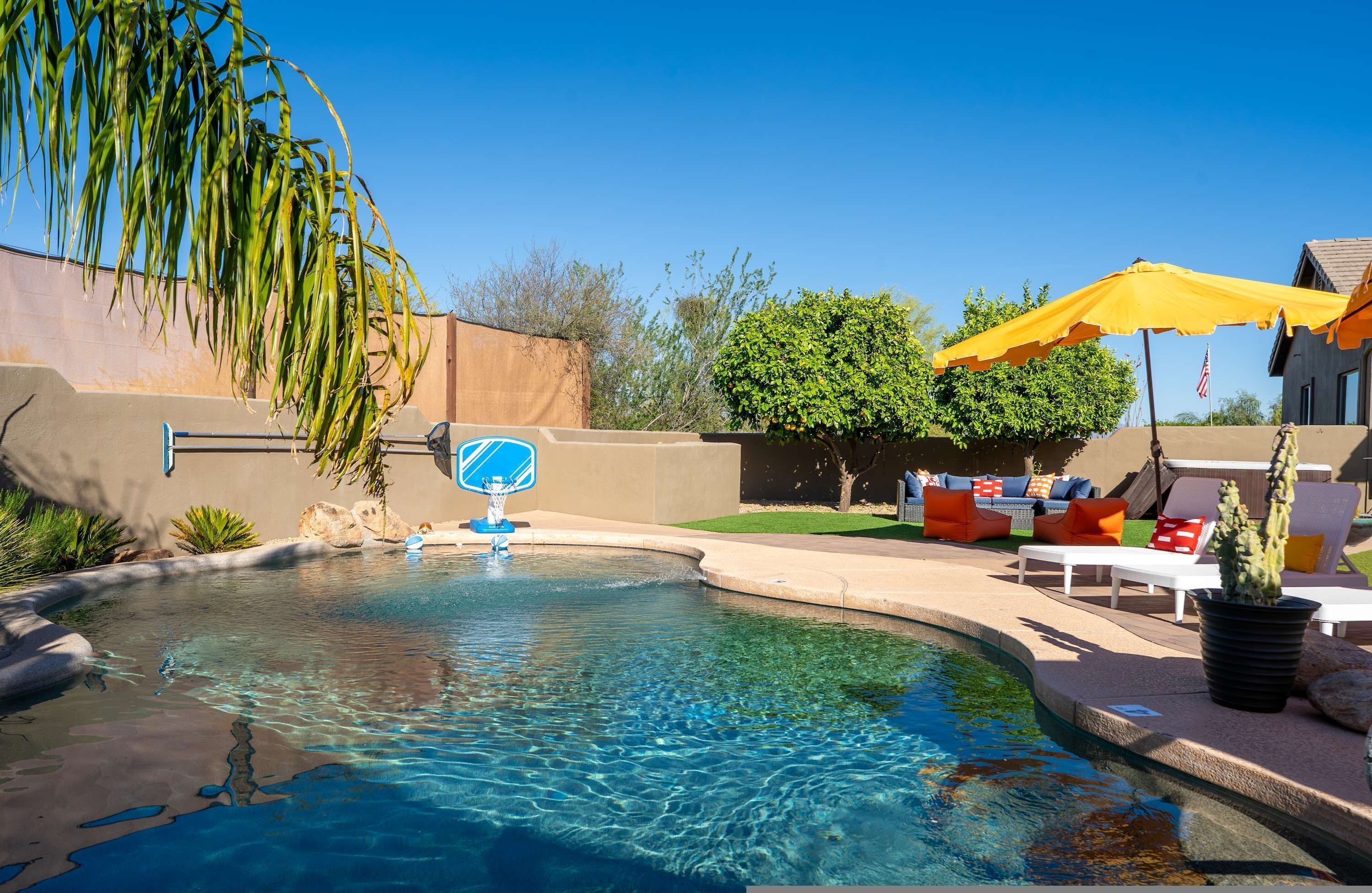 A clear swimming pool with a blue water feature, surrounded by a patio area with outdoor furniture and a cactus plant.