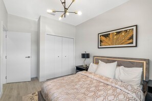 Ein modernes Schlafzimmer mit einem großen Bett, einem Nachttisch, einer Wandlampe und einem gerahmten Kunstwerk.