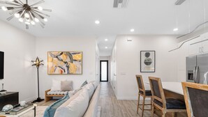 A modern living room with a sofa, a dining area with chairs, a kitchen with a refrigerator, and artwork on the walls. - Brand New Tampa Townhouse Prime Location (Tampa)