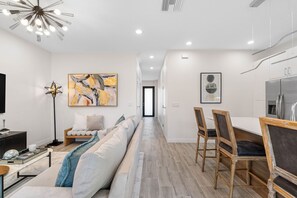 A modern living room with a sofa, a dining area with chairs, a kitchen with a refrigerator, and artwork on the walls. - Brand New Tampa Townhouse Prime Location (Tampa)