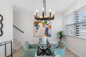 A modern dining area with a glass table surrounded by chairs, a contemporary chandelier, and a colorful abstract painting on the wall. - Brand New Tampa Townhouse Prime Location (Tampa)