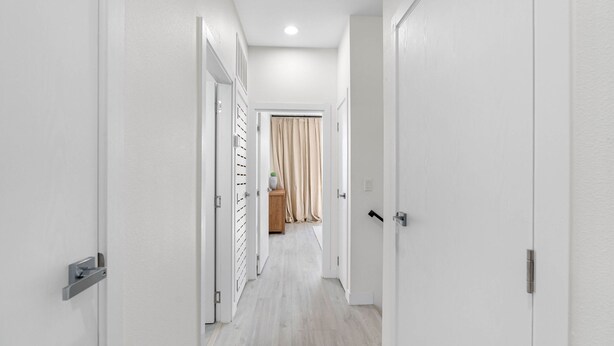 A hallway with white walls and doors, leading to a room with a wooden floor and a curtain. - Brand New Tampa Townhouse Prime Location (Tampa)