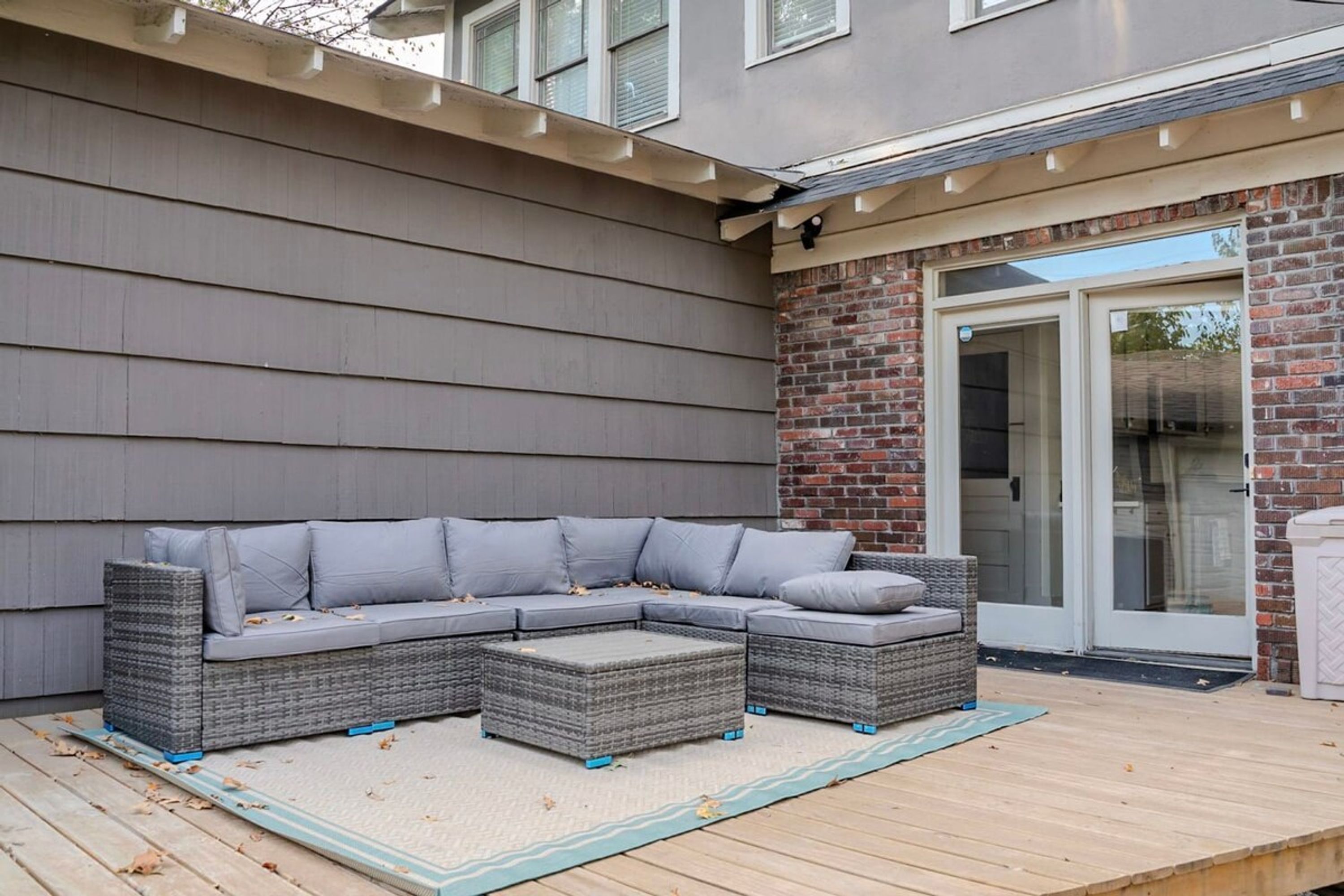 A sectional sofa with cushions on a deck, a brick wall, and a sliding glass door.