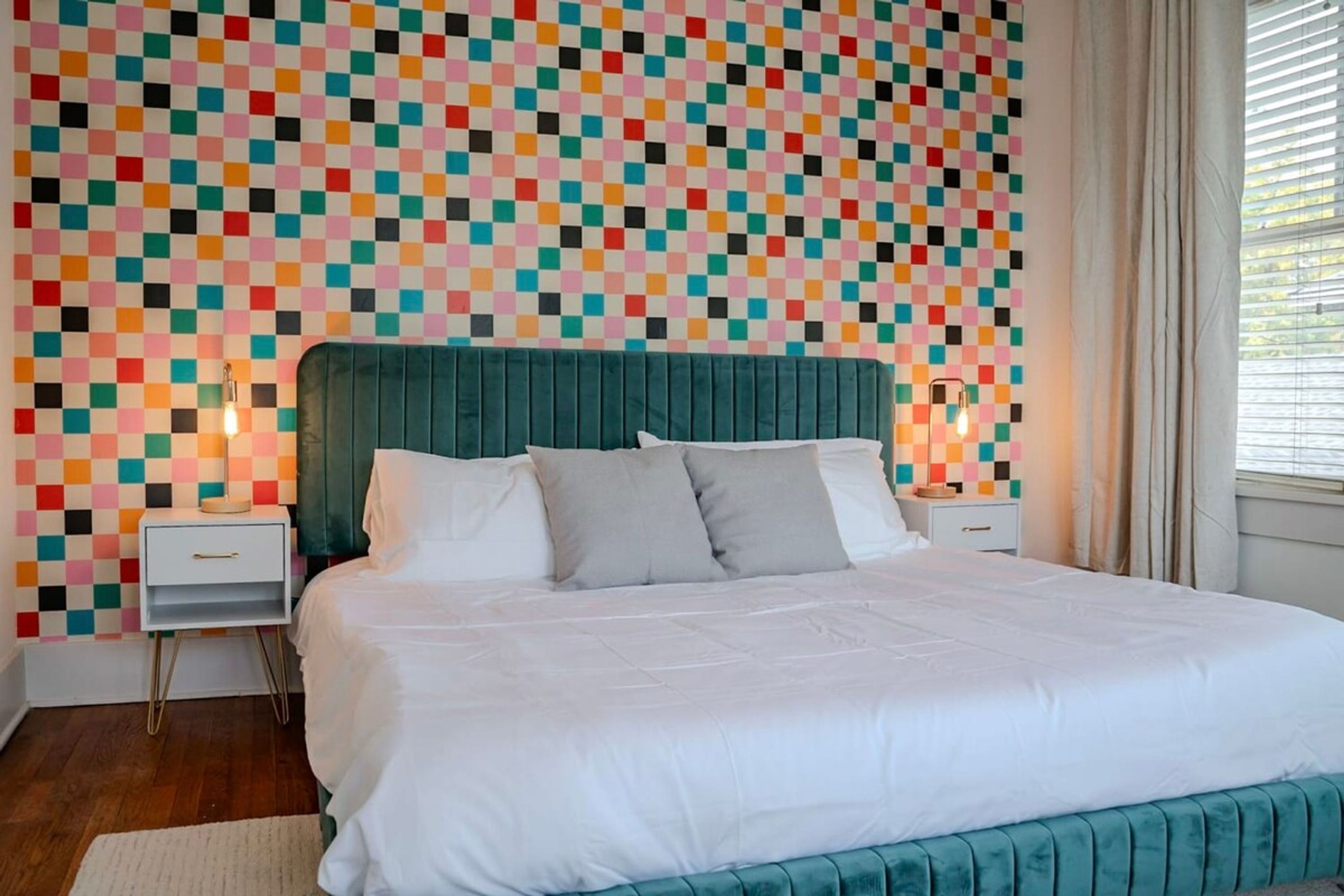 Un dormitorio con cabecera tapizada en color aguamarina, una colcha blanca y una pared con mosaicos de colores.