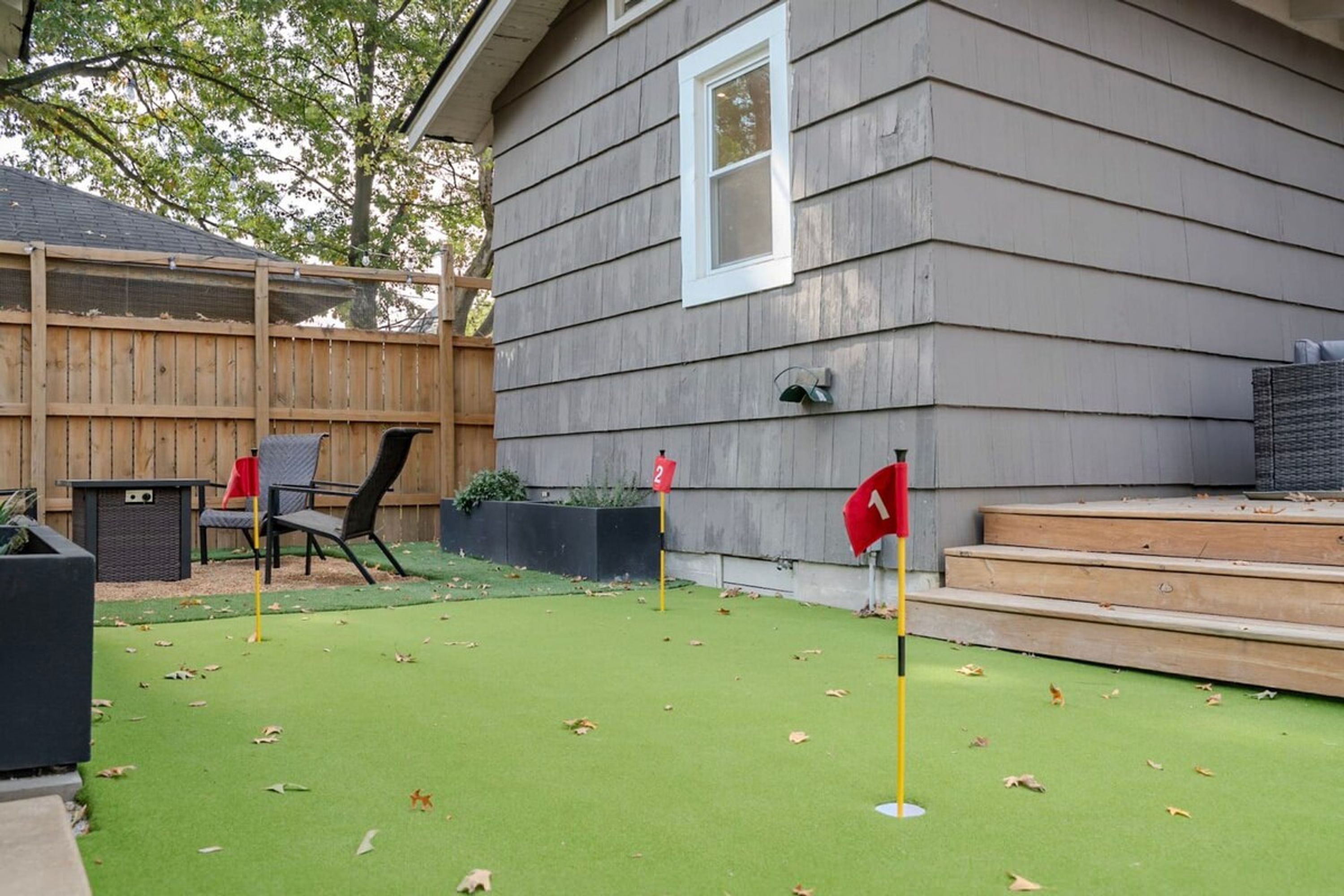 A backyard with artificial grass, a wooden deck, and a house with a window.