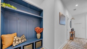 Ein Flur mit einer blauen Einbaubank, Aufbewahrungsbehältern, einer Vase mit orangefarbenen Blumen und einem Holztischchen mit Büchern.