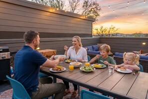 Una familia cenando al aire libre en una mesa de madera con vista al atardecer.