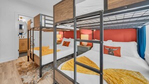 Ein Schlafraum mit Etagenbetten, einem Deckenventilator, einem Badezimmer mit Spiegel und einem gemusterten Teppich.