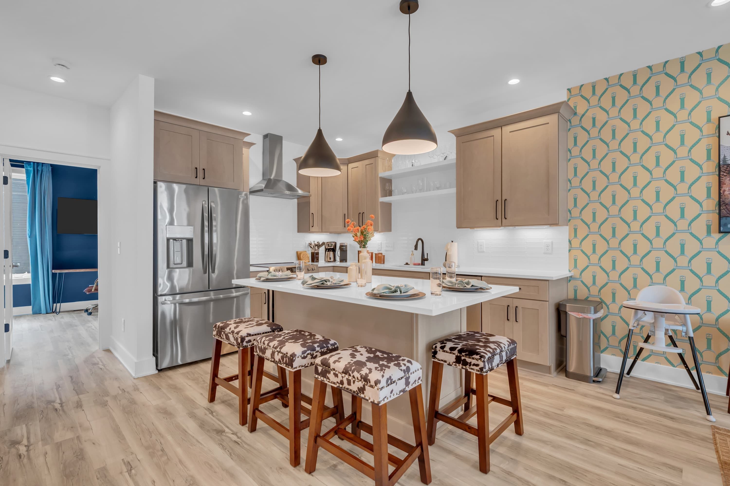 Cocina moderna con electrodomésticos de acero inoxidable, taburetes de madera y lámparas colgantes.
