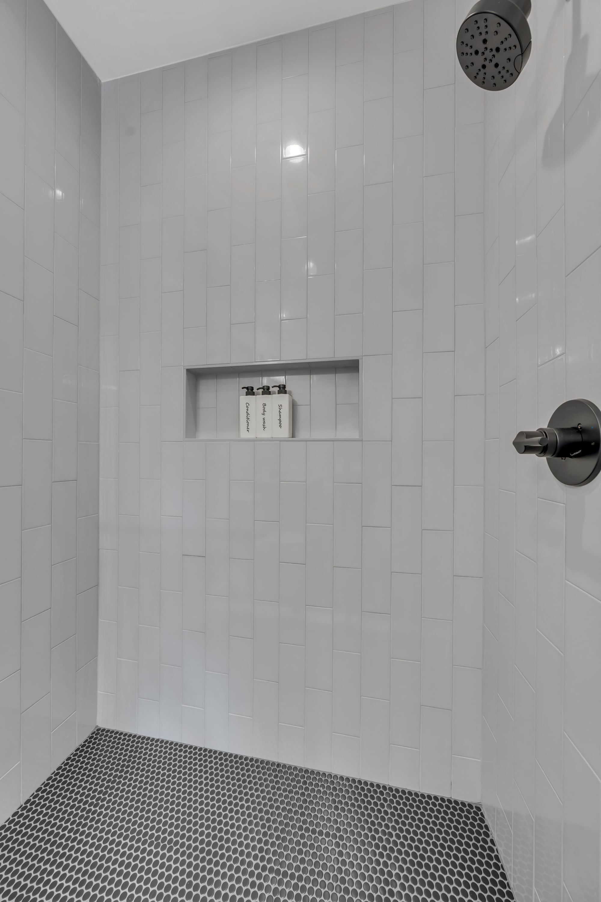 A modern shower with a control panel, a tiled floor, and a wall-mounted showerhead.
