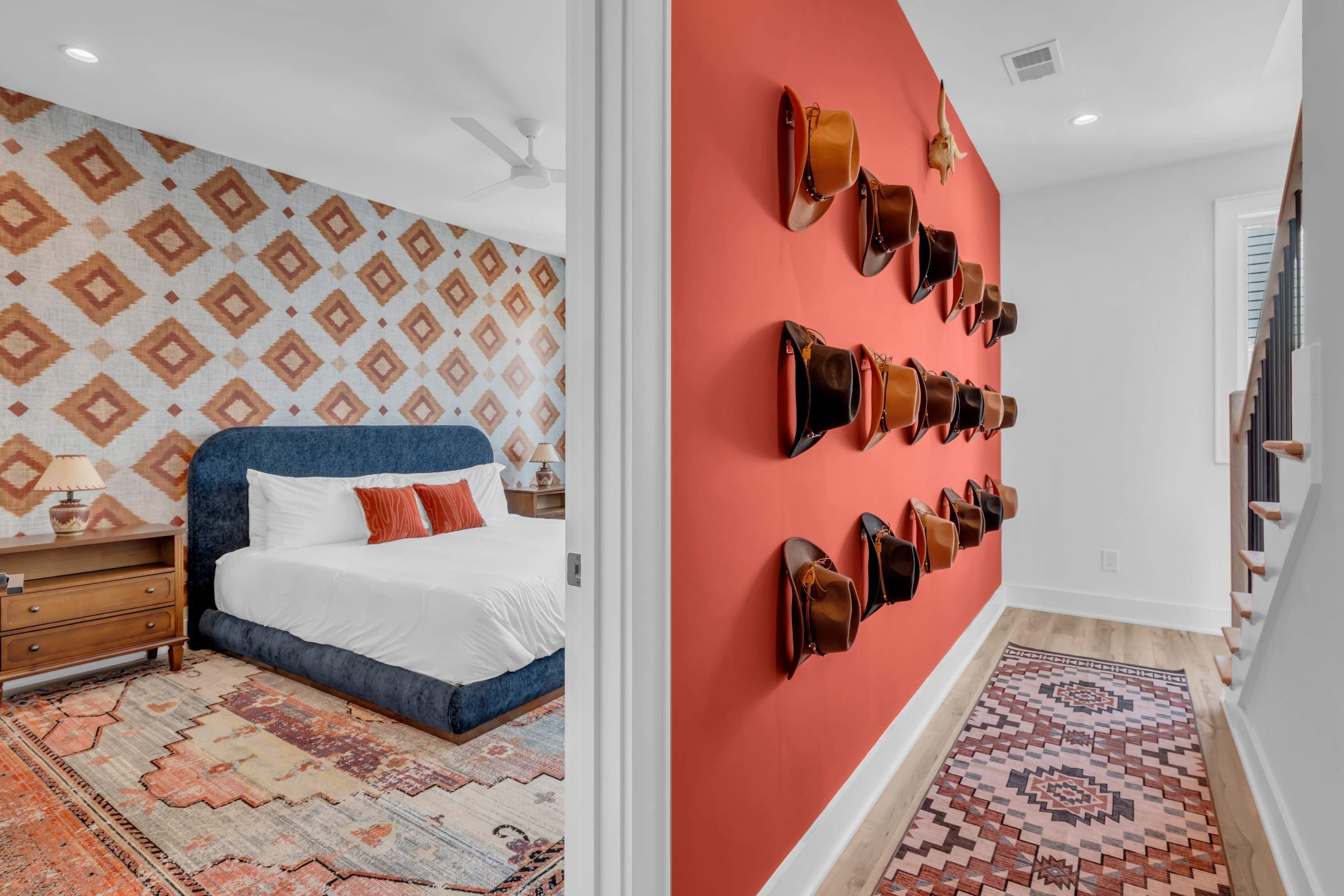 A hotel room with a patterned wall, a bed with white linens, a blue headboard, a nightstand, a lamp, and a wall-mounted shoe rack.
